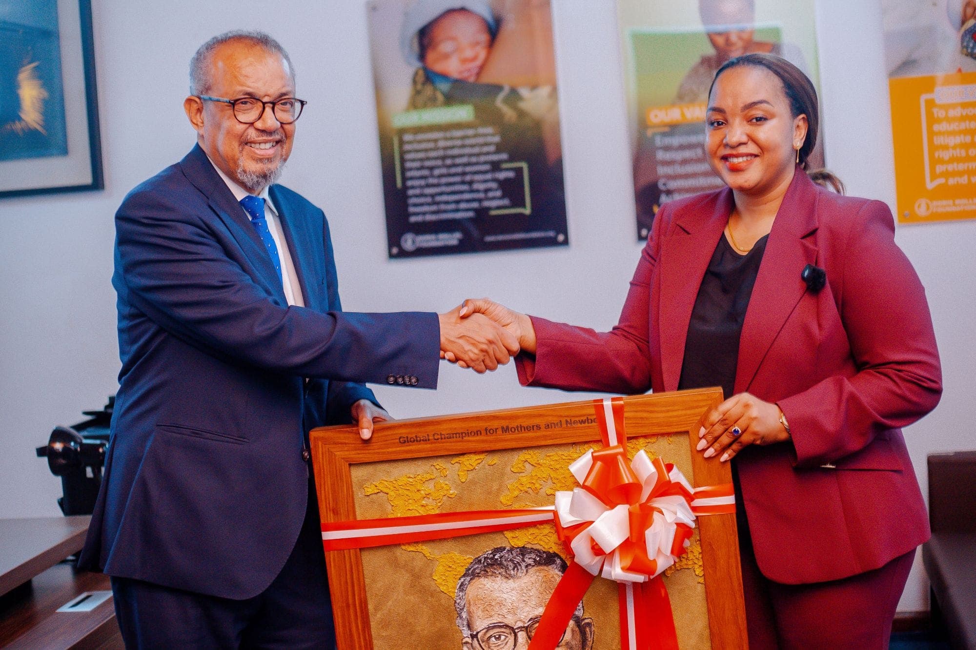 WHO Director-General Dr Tedros Adhanom Ghebreyesus shakes hands with Doris Mollel at the foundation's office, holding a framed portrait gift